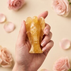 Citrine Angel Figurine held in hand with cream background and soft flower petals