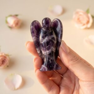 Amethyst Angel Figurine held in hand with cream background and soft flower petals