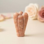 Sunstone Angel Figurine held in hand with cream background and soft flower petals