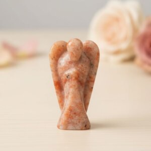 Sunstone Angel Figurine held in hand with cream background and soft flower petals