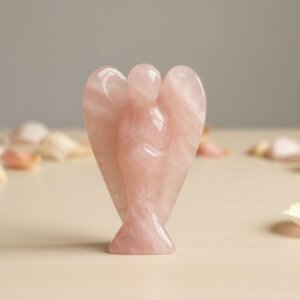 Rose Quartz Angel Figurine held in hand with cream background and soft flower petals