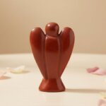 Red Jasper Angel Figurine held in hand with cream background and soft flower petals