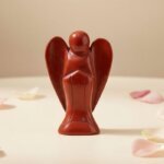 Red Jasper Angel Figurine held in hand with cream background and soft flower petals