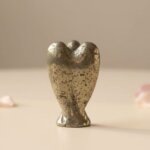 Pyrite Angel Figurine held in hand with cream background and soft flower petals