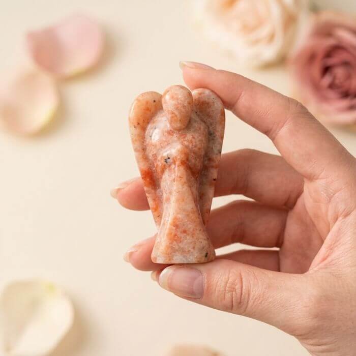 2 Sunstone Angel Figurine held in hand with cream background and soft flower petals