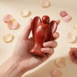 Red Jasper Angel Figurine held in hand with cream background and soft flower petals