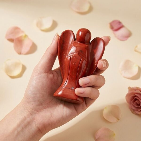 Red Jasper Angel Figurine held in hand with cream background and soft flower petals