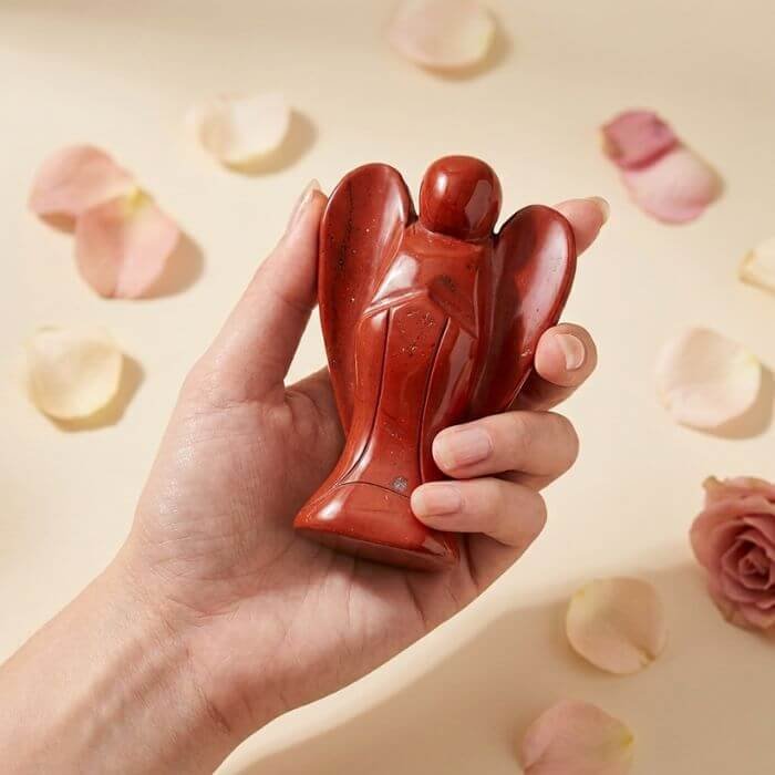 3 Red Jasper Angel Figurine held in hand with cream background and soft flower petals