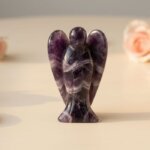 Amethyst Angel Figurine held in hand with cream background and soft flower petals