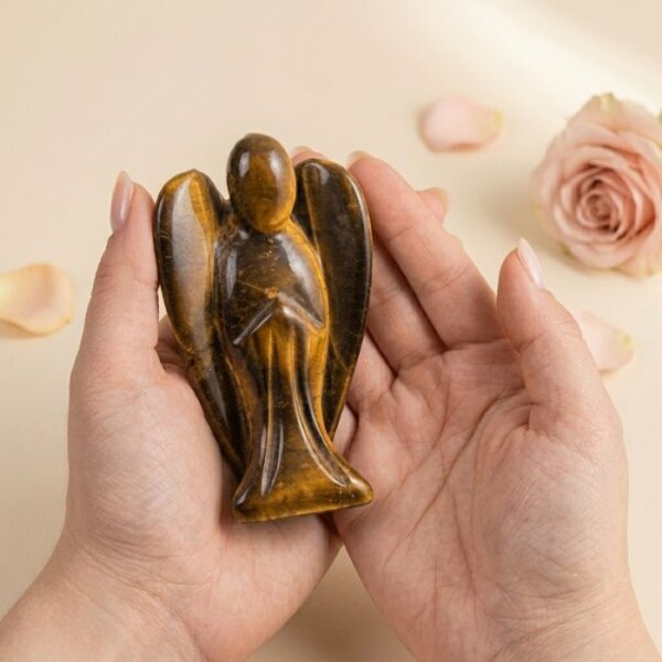 Tiger Eye Angel Figurine held in hand with cream background and soft flower petals