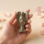 Pyrite Angel Figurine held in hand with cream background and soft flower petals