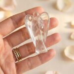 Clear Quartz Angel Figurine held in hand with cream background and soft flower petals