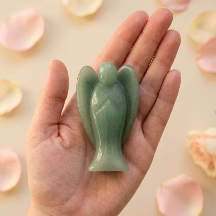 7 Green Aventurine Angel Figurine held in hand with cream background and soft flower petals