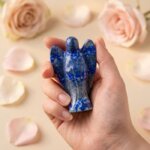 Lapis Lazuli Angel Figurine held in hand with cream background and soft flower petals