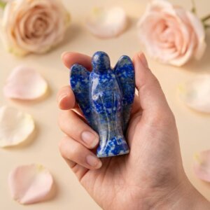 Lapis Lazuli Angel Figurine held in hand with cream background and soft flower petals