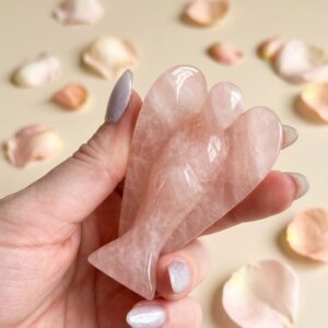 Rose Quartz Angel Figurine held in hand with cream background and soft flower petals