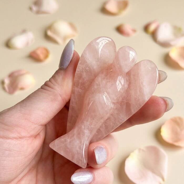 9 Rose Quartz Angel Figurine held in hand with cream background and soft flower petals